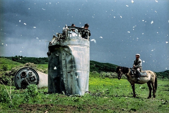 Jonas Bendiksen ~ Two boys scavenge copper wire from atop a crashed Soyuz spacecraft surrounded by white butterflies. A villager on horseback approaches to speak to them. Altai Territory, Russia